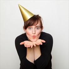 Studio Shot of young woman party hat blowing kiss. Photo : Jessica Peterson