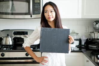 Smiling young woman holding black board in kitchen. Photo : Jessica Peterson