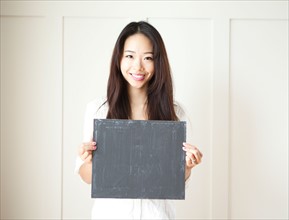Smiling young woman holding black board. Photo : Jessica Peterson