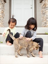 Two sisters (2-3, 4-5) playing with cat. Photo : Jessica Peterson