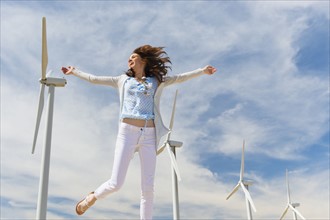 Woman jumping in front of wind turbines.
