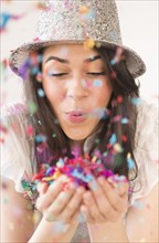 Portrait of young woman blowing confetti.