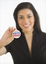 Studio portrait of young woman holding election badge.