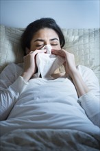 Young woman blowing nose in bed.