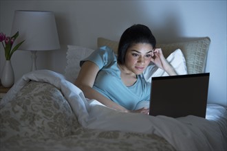 Young woman using laptop in bed.