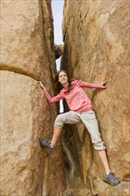 USA, California, Joshua Tree National Park, Young woman climbing canyon walls.