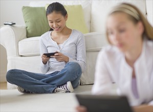 Two girls (14-17) relaxing at home using digital devices.