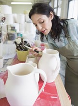 Female artist decorating pottery in studio.