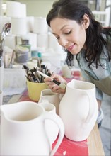 Female artist decorating pottery in studio.