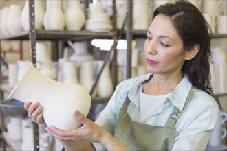 Woman holding vase in pottery warehouse.