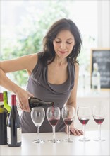 Woman purring red wine into wine glasses.