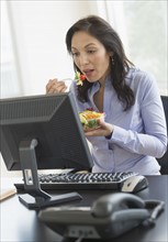 Business woman working on computer and eating salad.