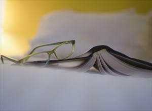 Book and eyeglasses on bed. 
Photo : Jamie Grill