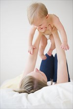 Mother lying on bed and lifting son (6-11 moths). 
Photo : Jamie Grill