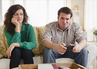 Couple sitting on sofa, man playing video game. 
Photo : Jamie Grill