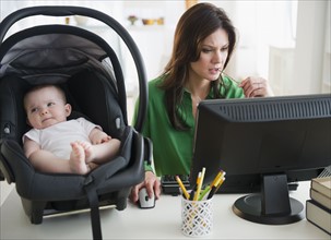 Mother working on computer, baby daughter (6-11 months) on desk. 
Photo: Jamie Grill
