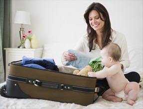 Mother with baby daughter (6-11 months) packing suitcase. 
Photo : Jamie Grill