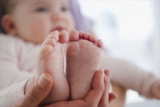 Close up of mother's hand holding baby daughter's (6-11 months) feet. 
Photo : Jamie Grill