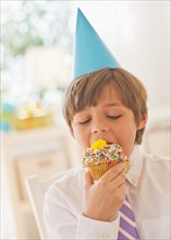 Portrait of boy (10-11 years) in party hat eating cupcake. 
Photo : Daniel Grill