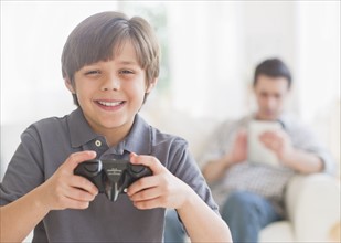 Boy (10-11 years) playing video game with father sitting in background. 
Photo : Daniel Grill