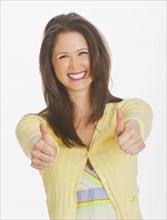 Portrait of smiling young woman showing thumbs up, studio shot. 
Photo: Daniel Grill