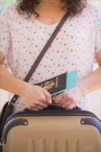Close up of woman holding luggage and passport. 
Photo : Daniel Grill