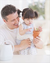 Baby girl (12-17 months) with father watching seedling in pot. 
Photo: Daniel Grill