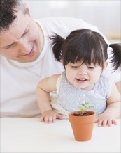 Baby girl (12-17 months) with father watching seedling in pot. 
Photo : Daniel Grill