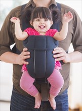 Baby girl (12-17 months) in baby carrier held by her father. 
Photo : Daniel Grill