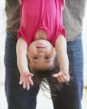 Father holding baby daughter (12-17 months) upside down. 
Photo : Daniel Grill