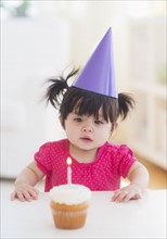 Portrait of baby girl (12-17 months) in party hat with cupcake. 
Photo : Daniel Grill