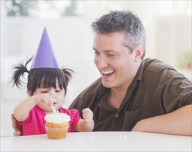 Portrait of father and baby girl (12-17 months) in party hat eating cupcake. 
Photo: Daniel Grill