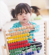 Portrait of baby girl (12-17 months) playing with abacus. 
Photo: Daniel Grill