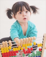 Portrait of baby girl (12-17 months) playing with abacus. 
Photo: Daniel Grill