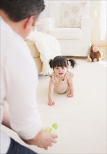 Father encouraging baby daughter (12-17 months) to crawl. 
Photo : Daniel Grill