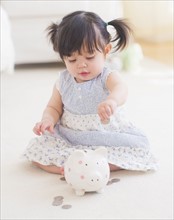Portrait of baby girl (12-17 months) playing with piggy bank. 
Photo: Daniel Grill