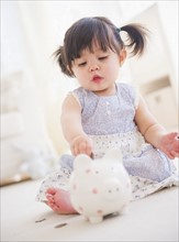 Portrait of baby girl (12-17 months) playing with piggy bank. 
Photo: Daniel Grill