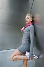 USA, California, Los Angeles, Young woman stretching near modern building.