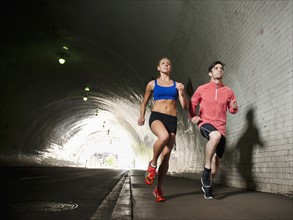 USA, California, Los Angeles, Young man and young woman running in tunnel.