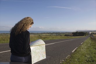France, Pas-de-Calais, Escalles, Young woman reading map on roadside. 
Photo : Jan Scherders