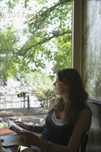 Holland, Amsterdam, Woman sitting with book in cafe window. 
Photo : Jan Scherders