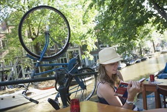 Holland, Amsterdam, Woman with guidebook sitting by canalside. 
Photo: Jan Scherders