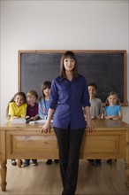 Teacher standing by desk with group of pupils. 
Photo : Rob Lewine