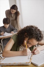 Writing girl (10-11) with boy (12-13) and teacher in background. 
Photo : Rob Lewine