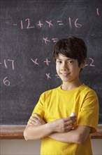 Portrait of schoolboy (12-13) standing in front of blackboard during math classes. 
Photo: Rob