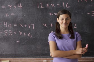 Portrait of schoolgirl (12-13) standing in front of blackboard during math classes. 
Photo: Rob