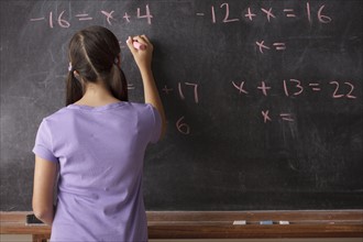 Portrait of schoolgirl (12-13) standing in front of blackboard during math classes. 
Photo : Rob
