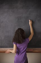 Portrait of schoolgirl (10-11) writing on blackboard. 
Photo : Rob Lewine