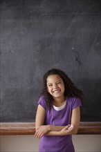 Portrait of schoolgirl (10-11) standing in front of blackboard. 
Photo : Rob Lewine