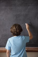 Rear view of schoolboy (10-11) writing on blackboard. 
Photo : Rob Lewine